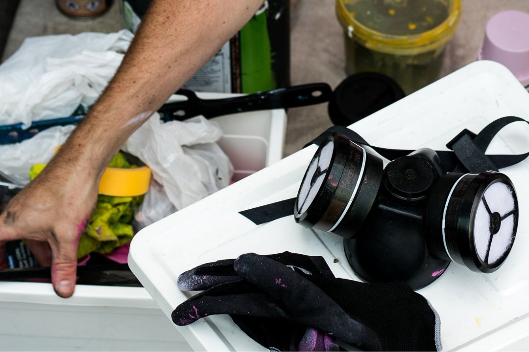 A respirator and gloves next to chemical containers