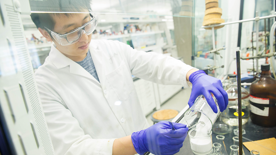 Man working in a lab, wearing gloves, goggles and a lab coat